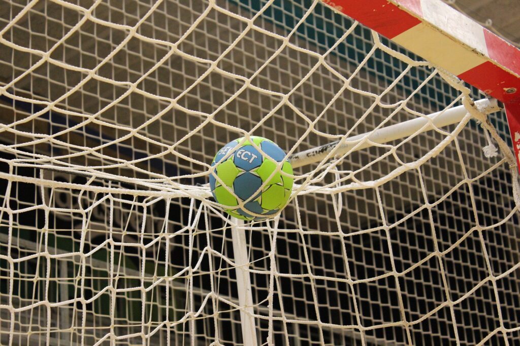 Ein Handball ist im Netz eines Tores gefangen, ein Zeichen für ein erfolgreiches Spiel.