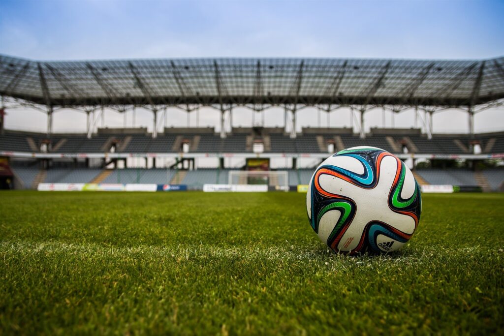 Ein Fußball liegt auf dem Gras vor einem leeren Stadion, bereit für das nächste Spiel