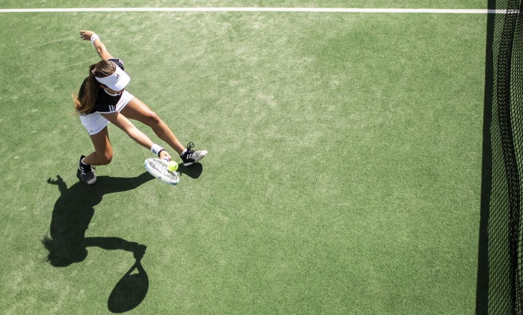 Eine Frau schlägt den Tennisball auf einem grünen Platz und hat viel Spaß dabei.